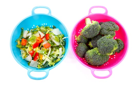 Two colorful colanders with vegetables over white background