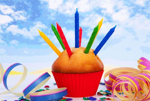 Birthday cupcake with lots of candles and colorful confetti over cloudy background