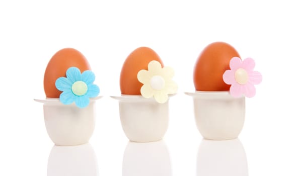 Three chicken eggs in holder with flowers over white background