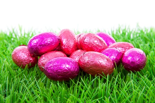 Pink chocolate easter eggs on grass over white background