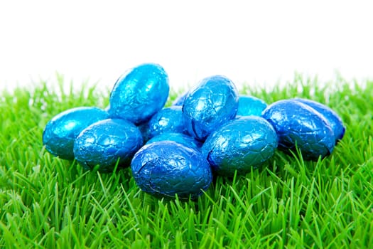 Blue chocolate easter eggs on grass over white background