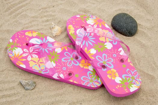 pink colored summer slippers lying on sand