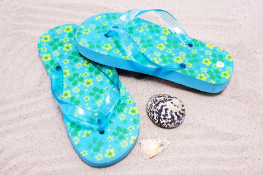 Blue colored summer slippers lying on sand