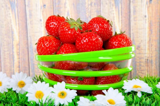 Bowl with fresh strawberries on grass over wooden background