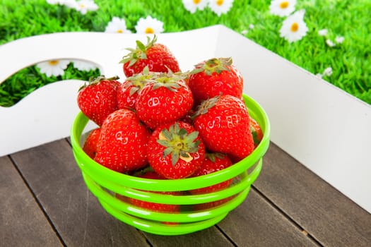 Bowl with fresh strawberries on tray against grass background