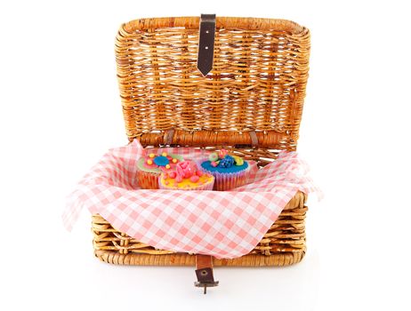 Picnic basket with decorated cupcakes over white background