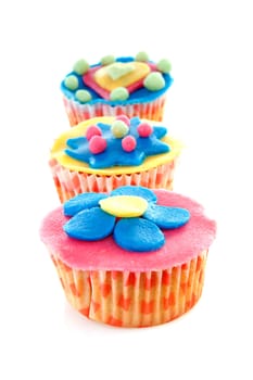 three cupcakes in a row with marzipan decoration over white background