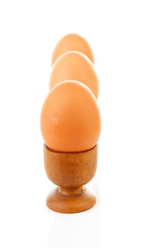 Three chicken eggs in wooden holder over white background