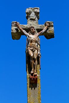 Statue of Jesus on a stone cross over blue background
