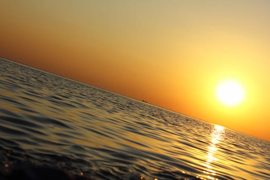 Sea sunset, inclined view with ship on horizon.