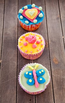 three cupcakes with marzipan decoration on wooden background