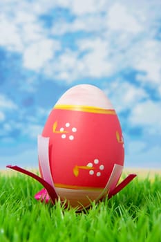Pink easter egg on grass against sky and clouds