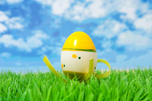 Yellow easter egg on grass against sky and clouds