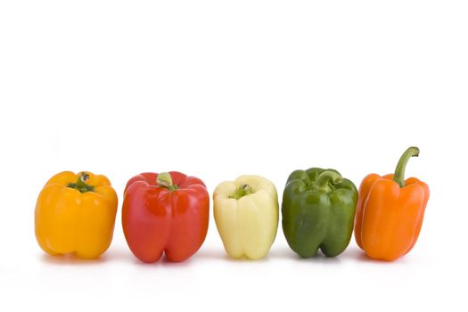 Five different coloured peppers in a row isolated on white