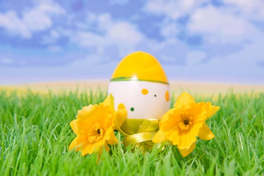plastic easter egg on grass with flowers with behind it blue sky and clouds