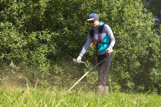 boy working on a trimmer in a sunny summer day 