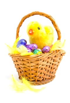 Cane basket with colorful chocolate easter eggs and yellow little chicken over white background