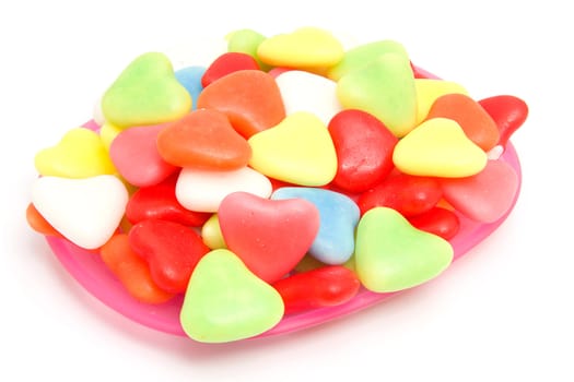 Pink plate with colorful candy in shape of hearts over white background