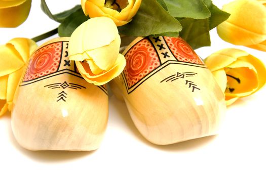 Typical Dutch wooden shoes with silk yellow tulips over white background