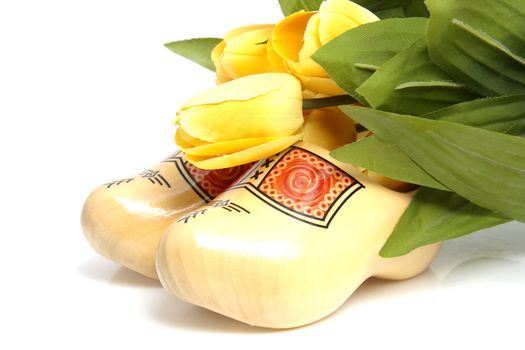 Typical Dutch wooden shoes with silk yellow tulips over white background