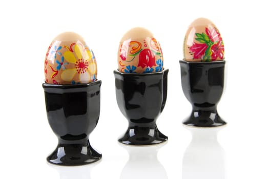 Three decorated chicken eggs in black holder over white background