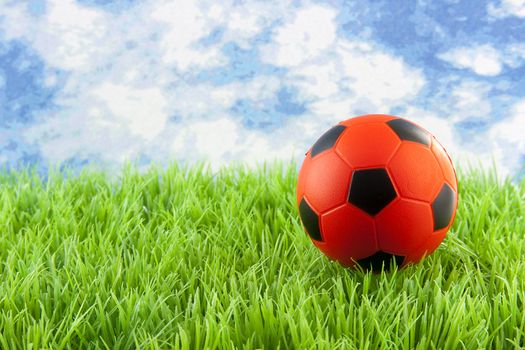 orange Soccer ball on grass against blue cloudy sky