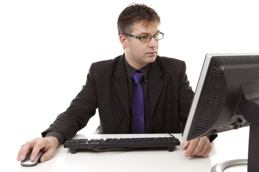 Businessman sitting behind desk at work, looking at monitor, over white background