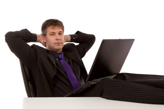 Businessman is sitting relaxed with feet on desk, looking in camera over white background