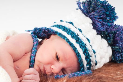 Shot of newborn baby lying on fur in knitted hat with pom-pons