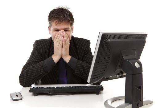 Businessman sitting behind desk is in despair, covering his mouth, over white background