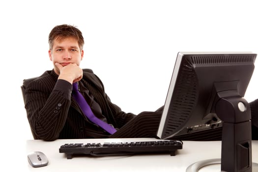 Businessman sitting with feet on his desk is looking at you over white background