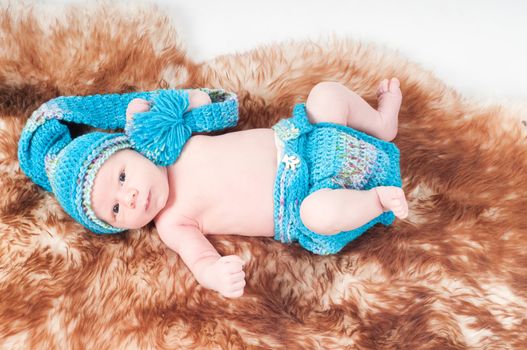 Shot of newborn baby in knitted blue clothes lying on fur