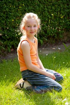 Little blonde girl is sitting in grass looking at camera