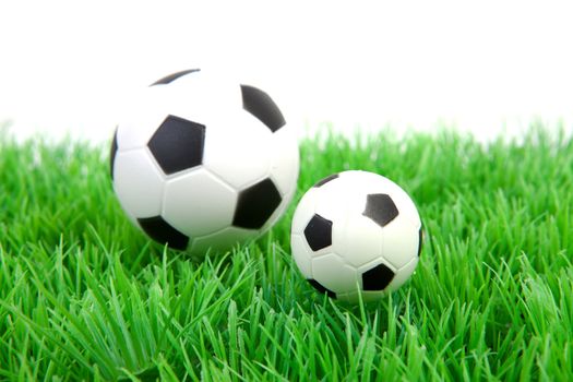 One big and one little soccer ball on grass over white background