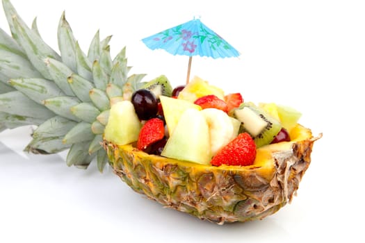 Hollowed pineapple filled with fresh summer fruits over white background