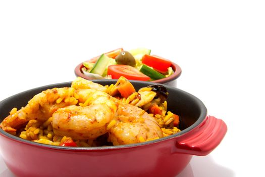 little casserole with paella and sea food over white background, behind it a bowl with salad