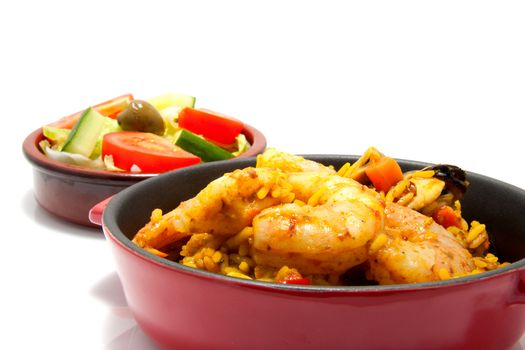 little casserole with paella and sea food over white background, behind it a bowl with salad