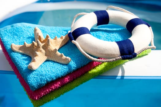 summer gear; colorful towel, life buoy and starfish by the swimpool