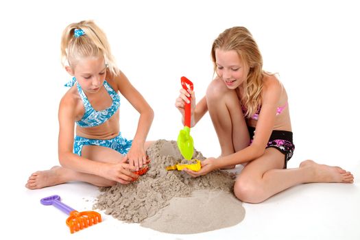Young blonde girls in beach wear playing with sand over white background