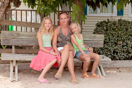 Mother and daughters sitting on a wooden bench under some trees