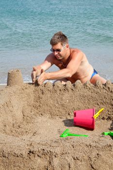 man is making sand castle on the beach near the sea