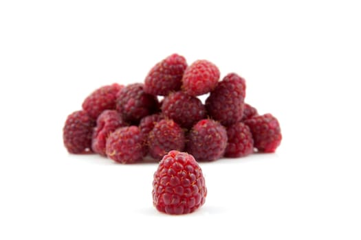 pile of fresh raspberries with focus on one berry in the front over white background