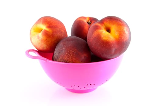 pink plastic colander with fresh peaches over white background
