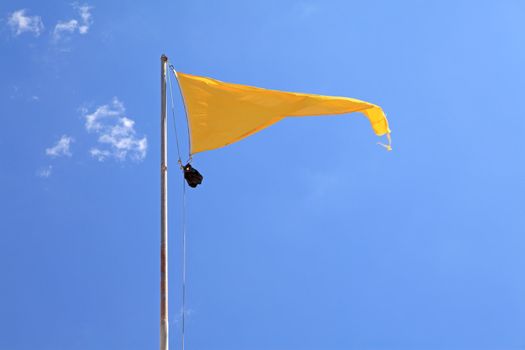 yellow warning flag on the beach against blue sky