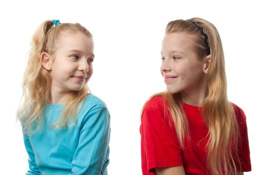 Two blonde girls sitting back to back, looking at each other, over white background