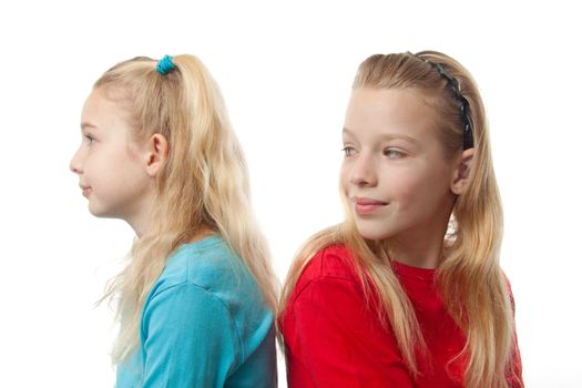 Two blonde girls sitting back to back, one is looking at the other, over white background