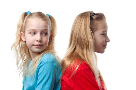 Two blonde girls sitting back to back, one is looking at the other, over white background