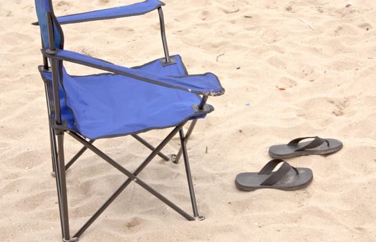 Folding chair and slippers at the beach of the sea.