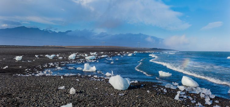 Beautiful beach in the South of Iceland with a black lava sand is full of icebergs from glaciers not far away. Panorama