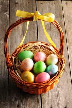 Colored easter eggs in basket on wooden table